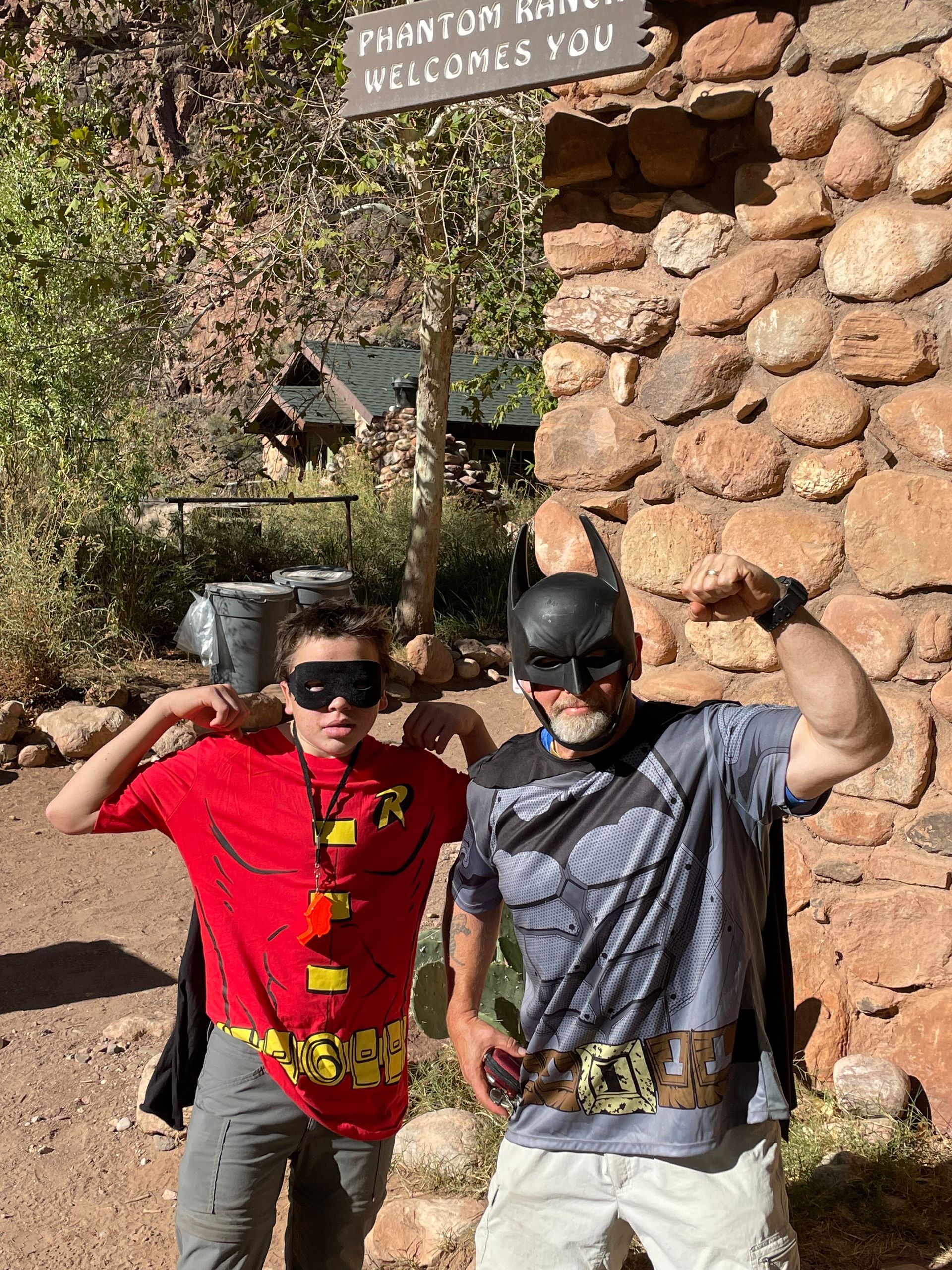 Two men dressed as batman and robin are posing for a picture in front of a stone wall.