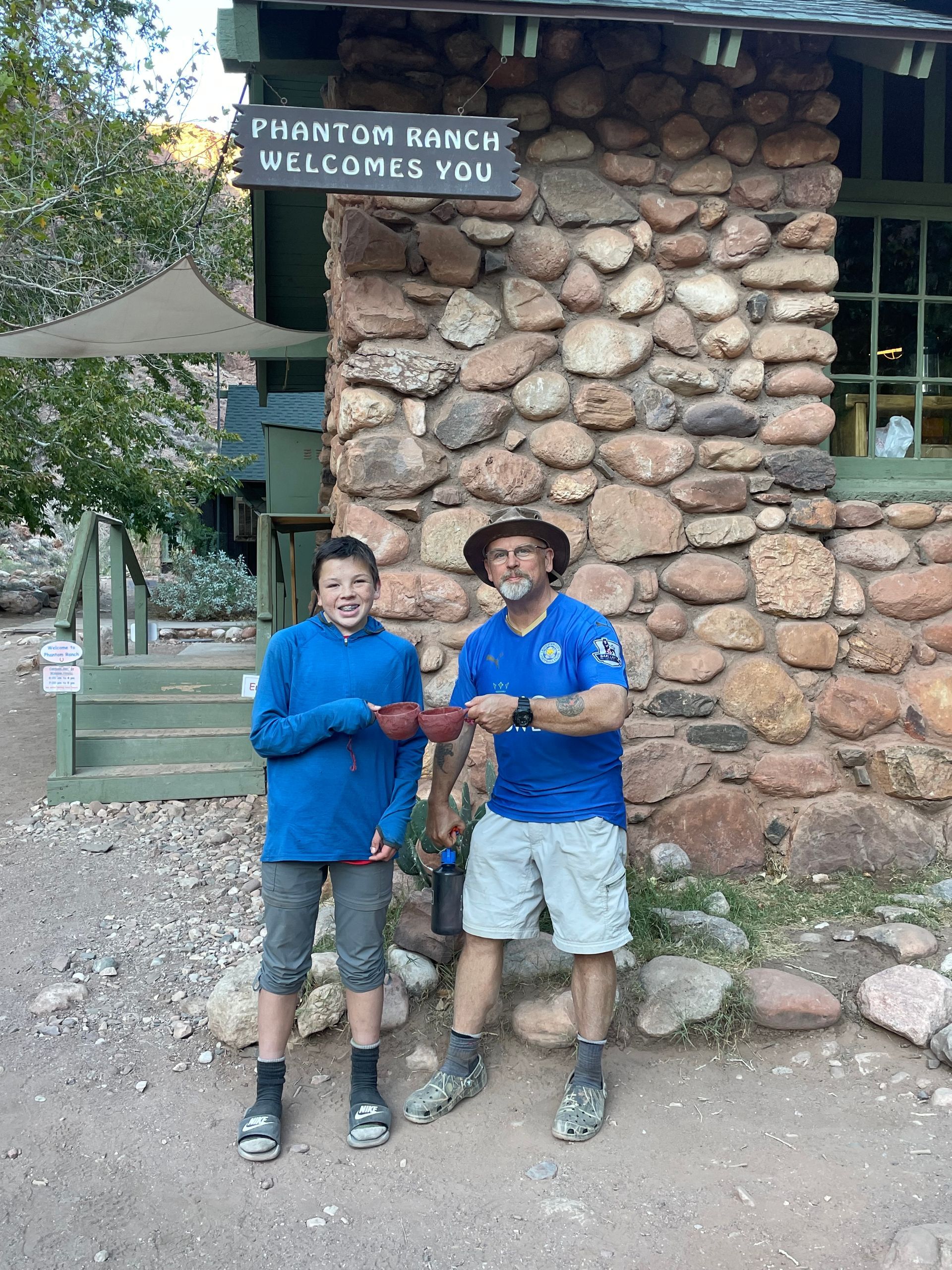 A man and a boy are standing in front of a stone building.