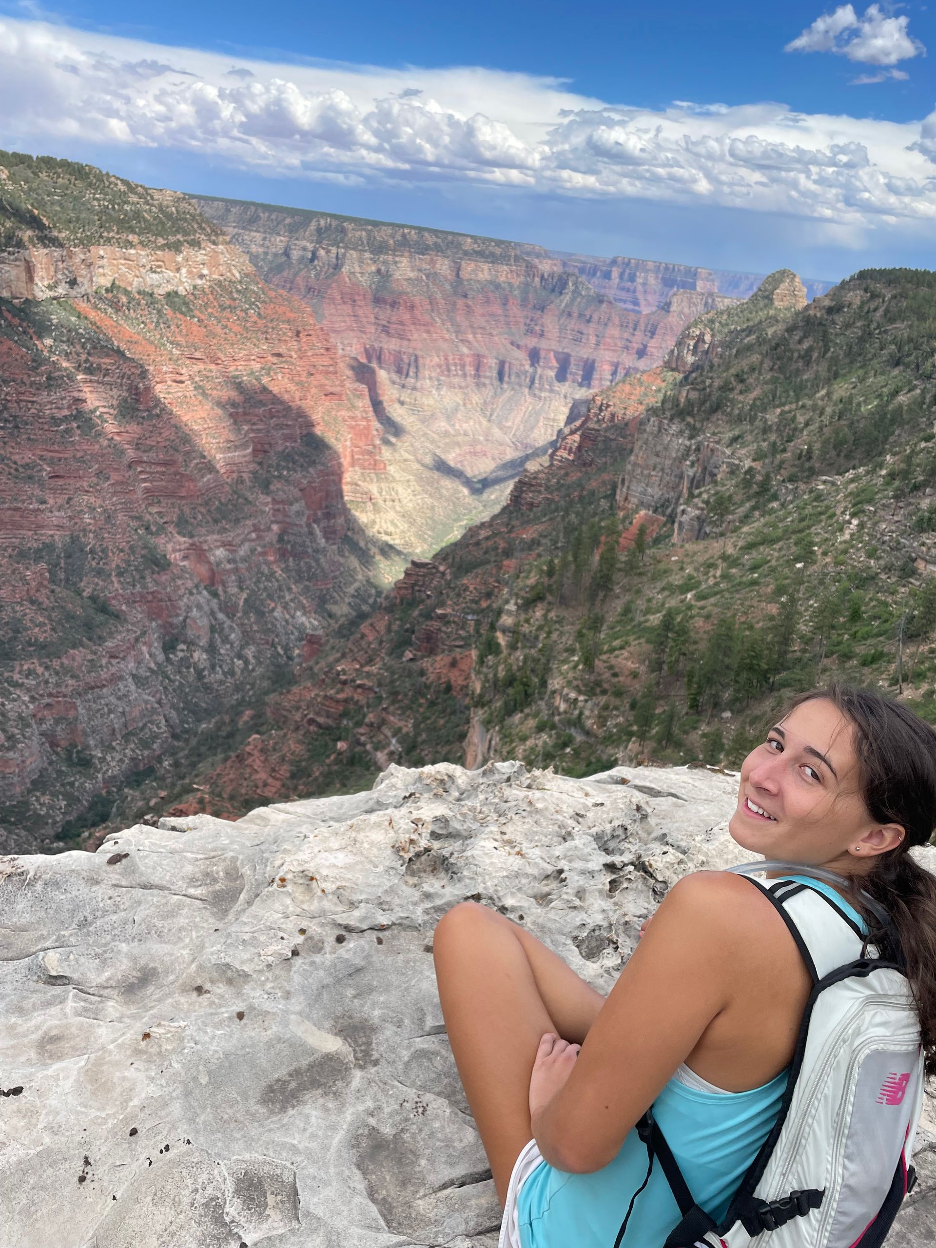 A woman is sitting on the edge of a cliff overlooking a canyon.