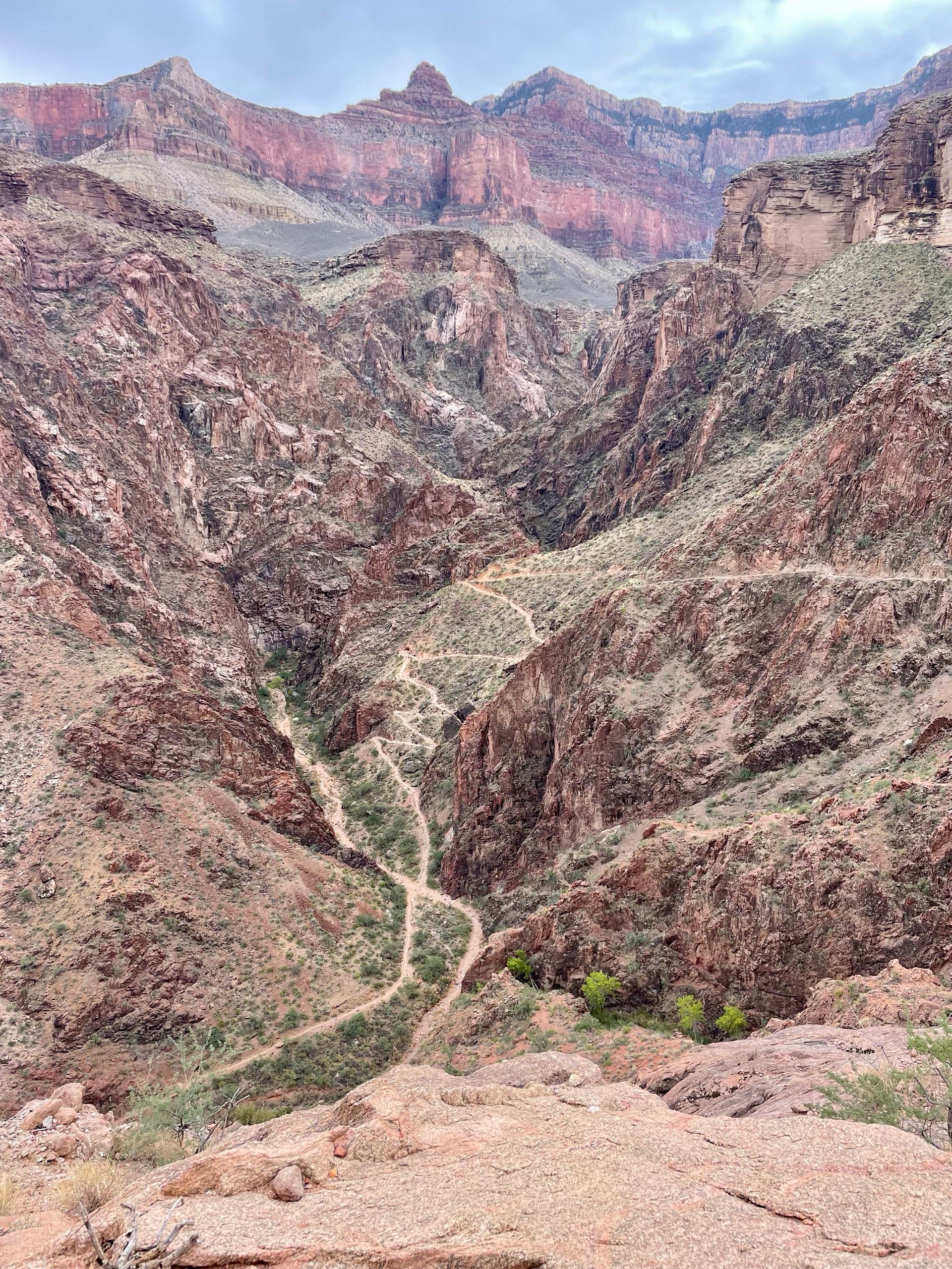 A view of a canyon with mountains in the background and a dirt road going through it.