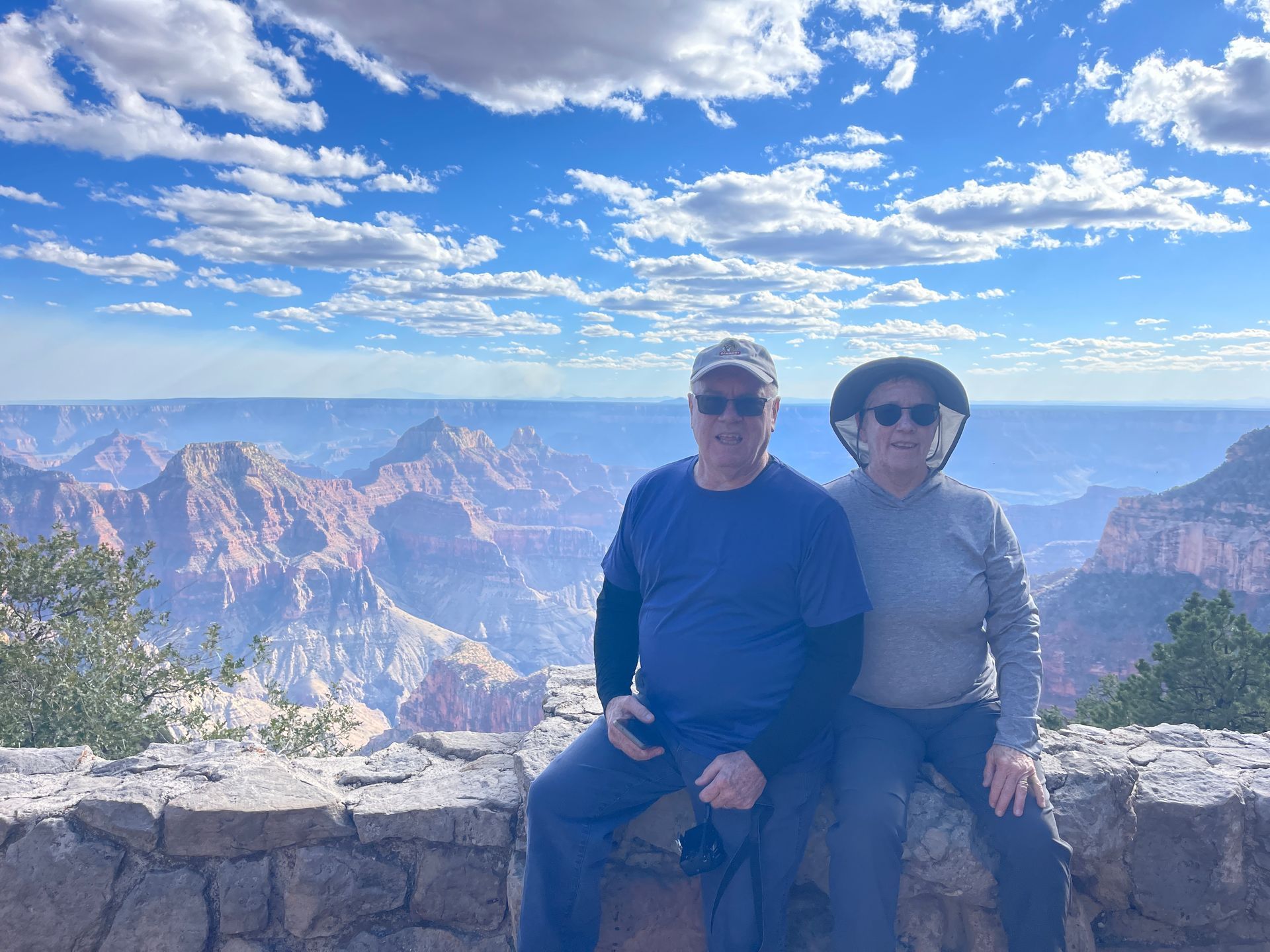 A man and a woman are sitting on a stone wall overlooking the grand canyon.