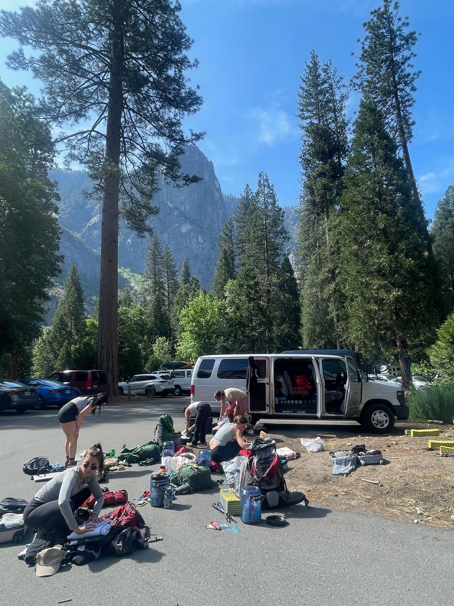 A group of people are gathered in a parking lot with a van parked in the background.