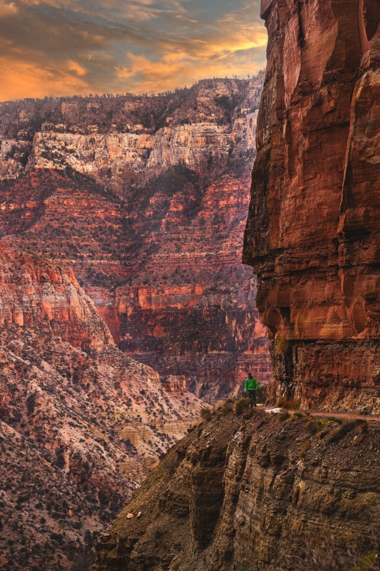 A person is sitting on the edge of a cliff overlooking a canyon.