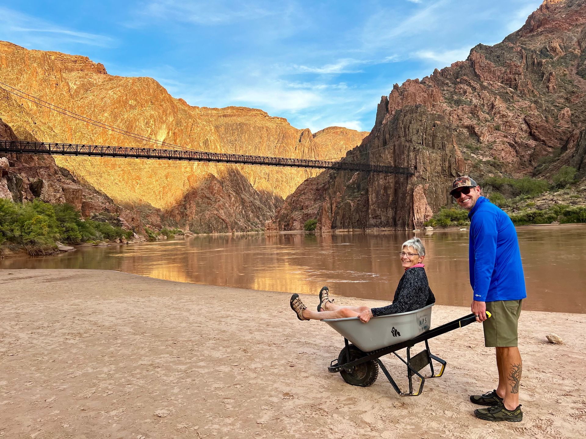 A man is pushing a wheelbarrow with a person in it.
