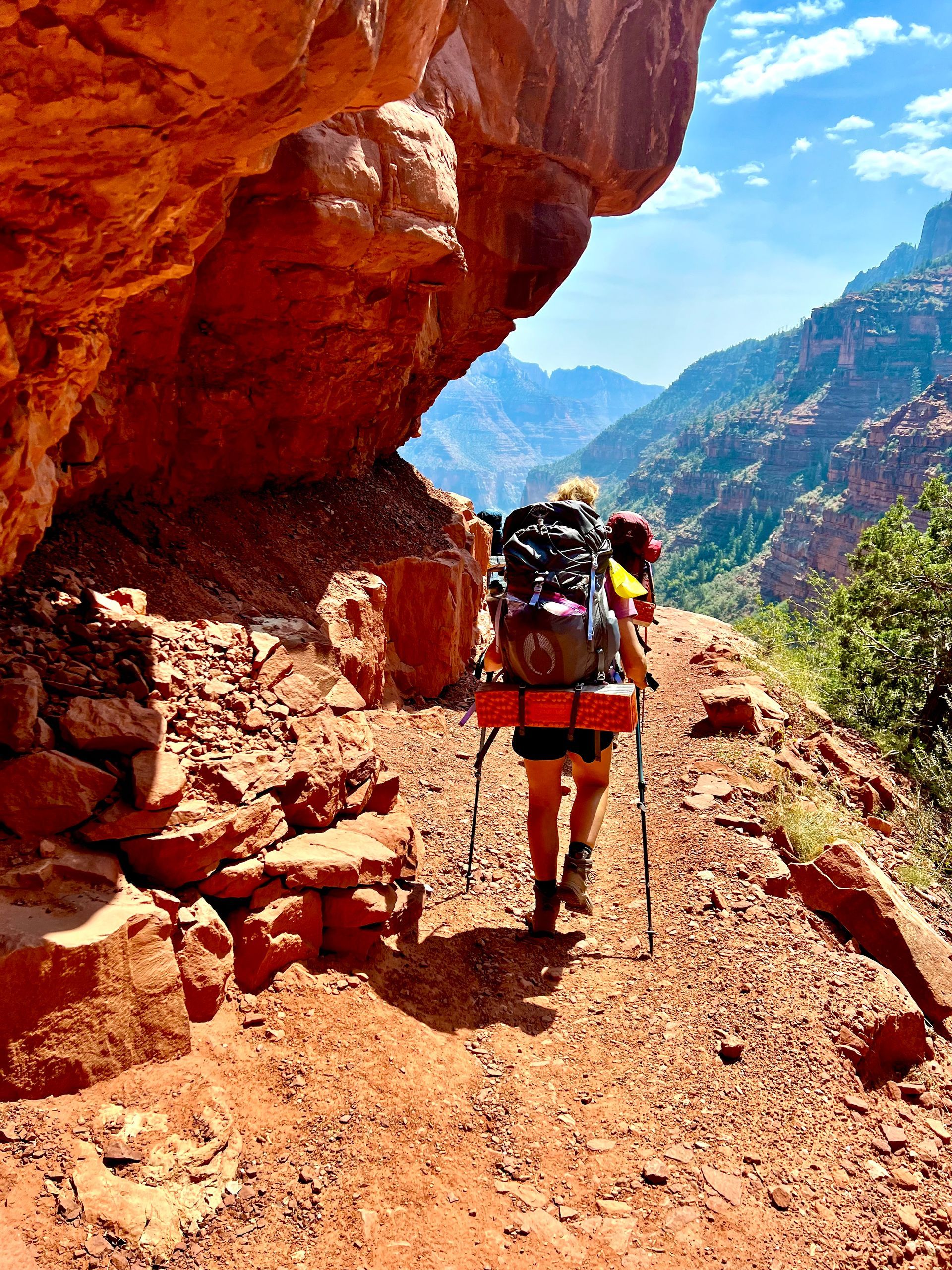 A person with a backpack is walking down a trail in the mountains.