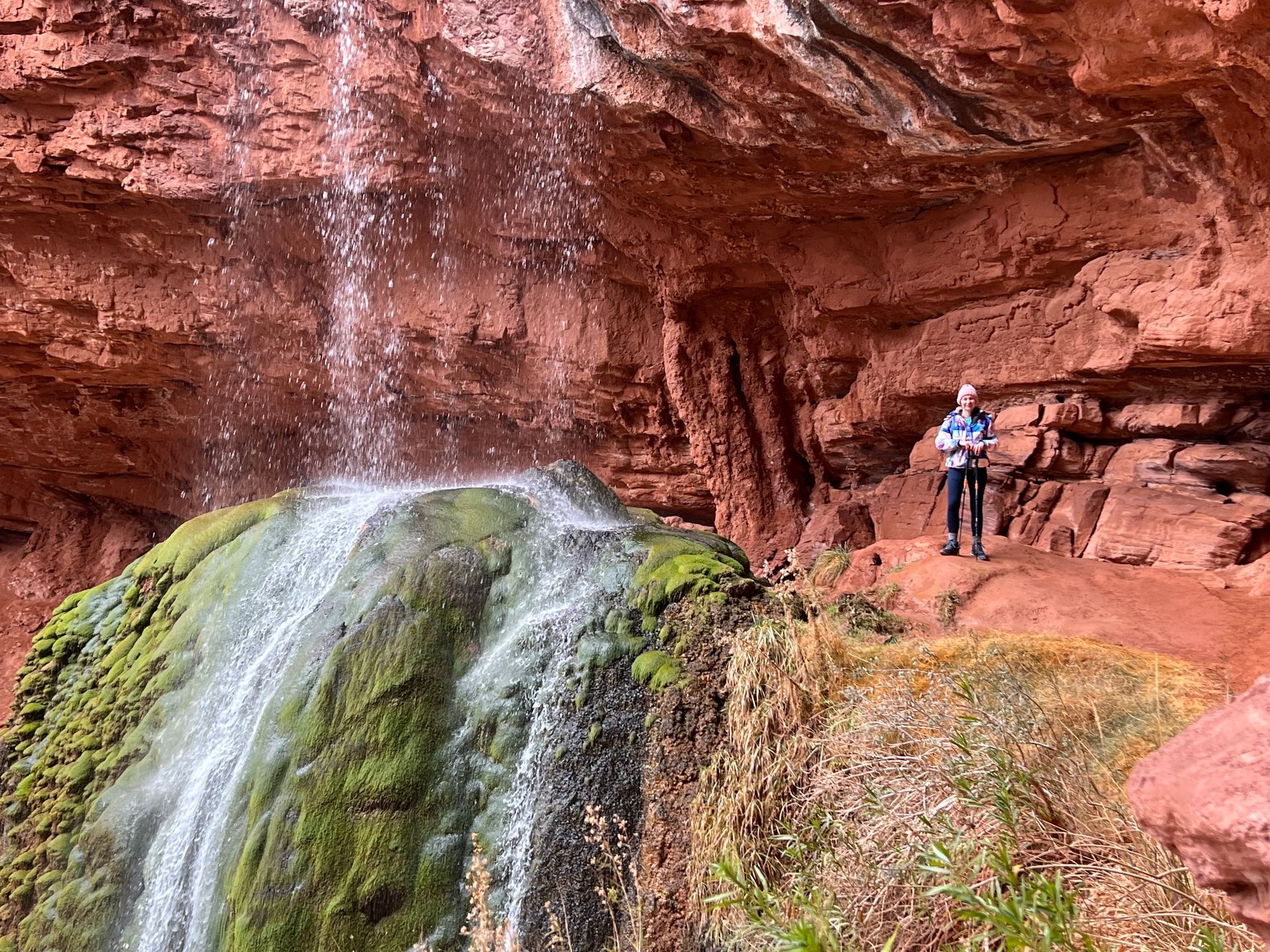 A man is standing in front of a waterfall in the desert.