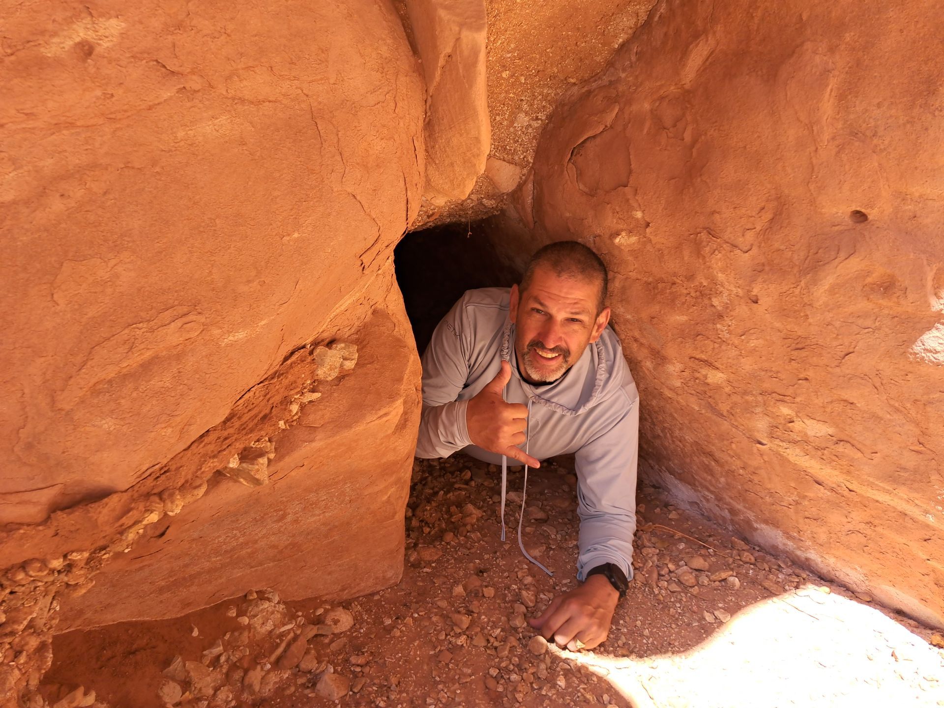 A man is crawling out of a cave and giving a thumbs up.