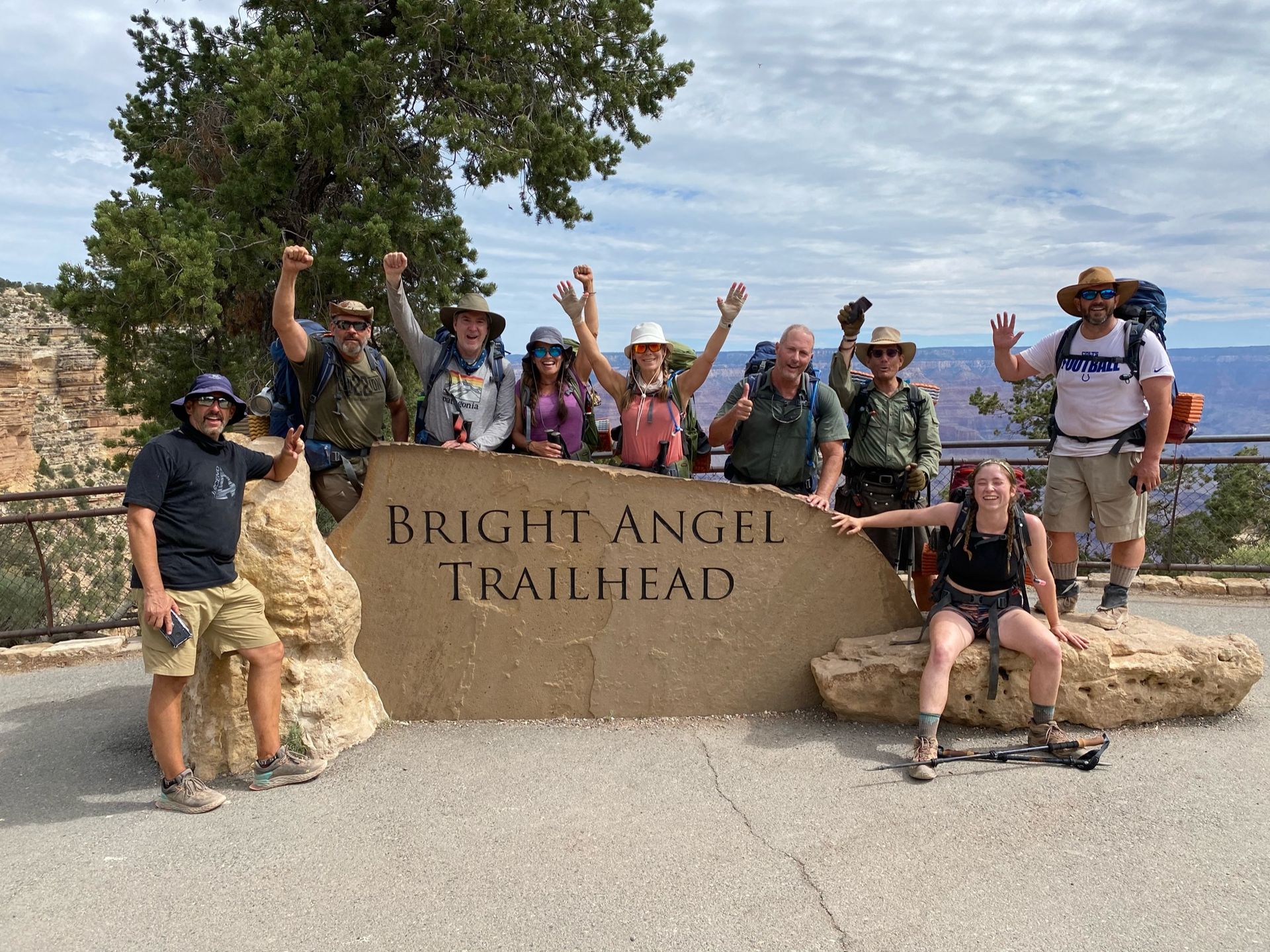 A group of people are posing for a picture in front of a sign that says bright angel trailhead.