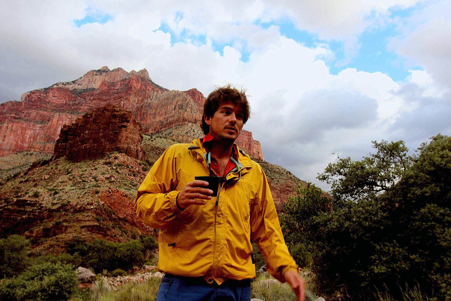 A man in a yellow jacket is standing in front of a mountain.