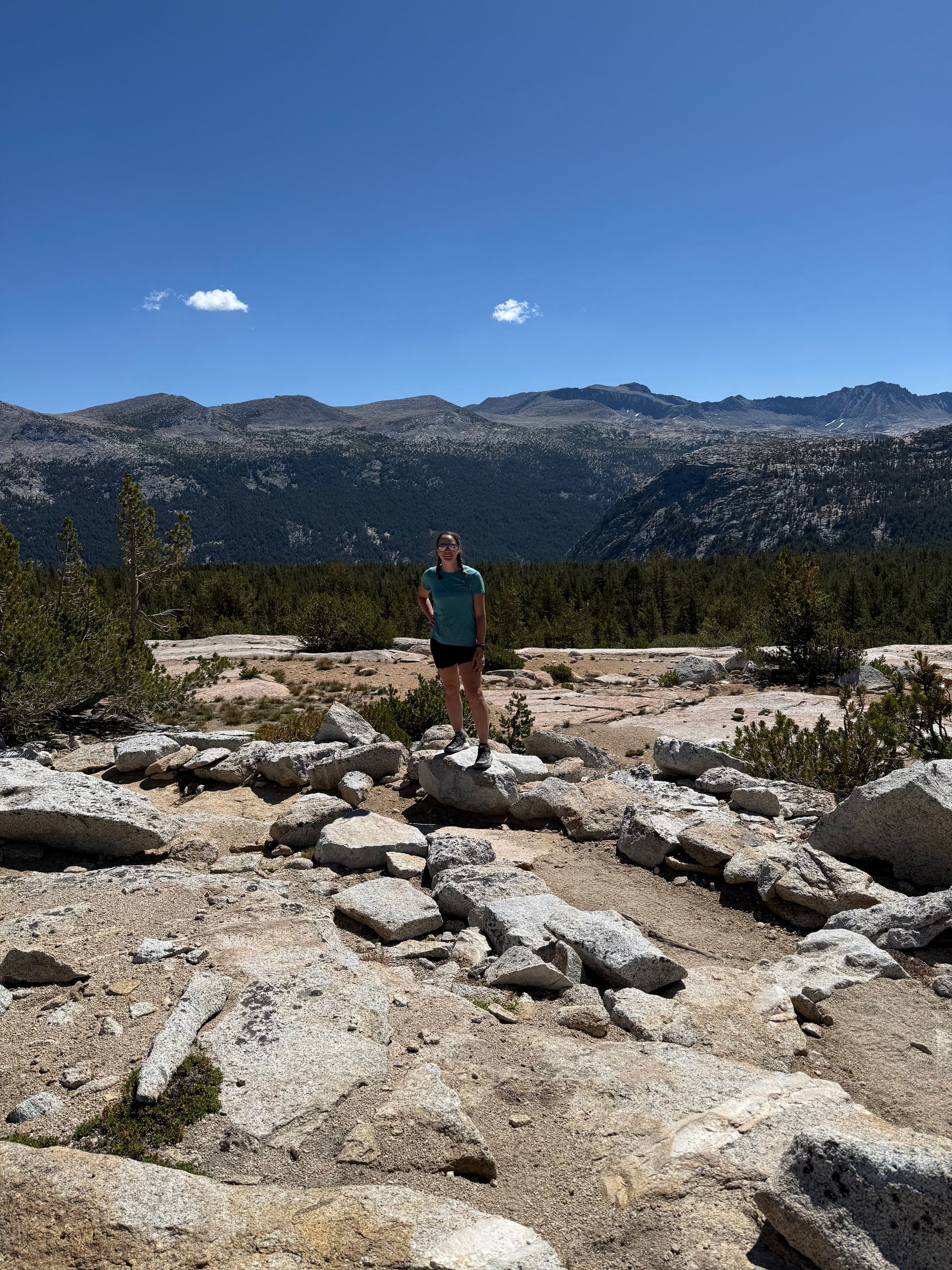 Woman standing on rocks, mountain backdrop, blue sky.