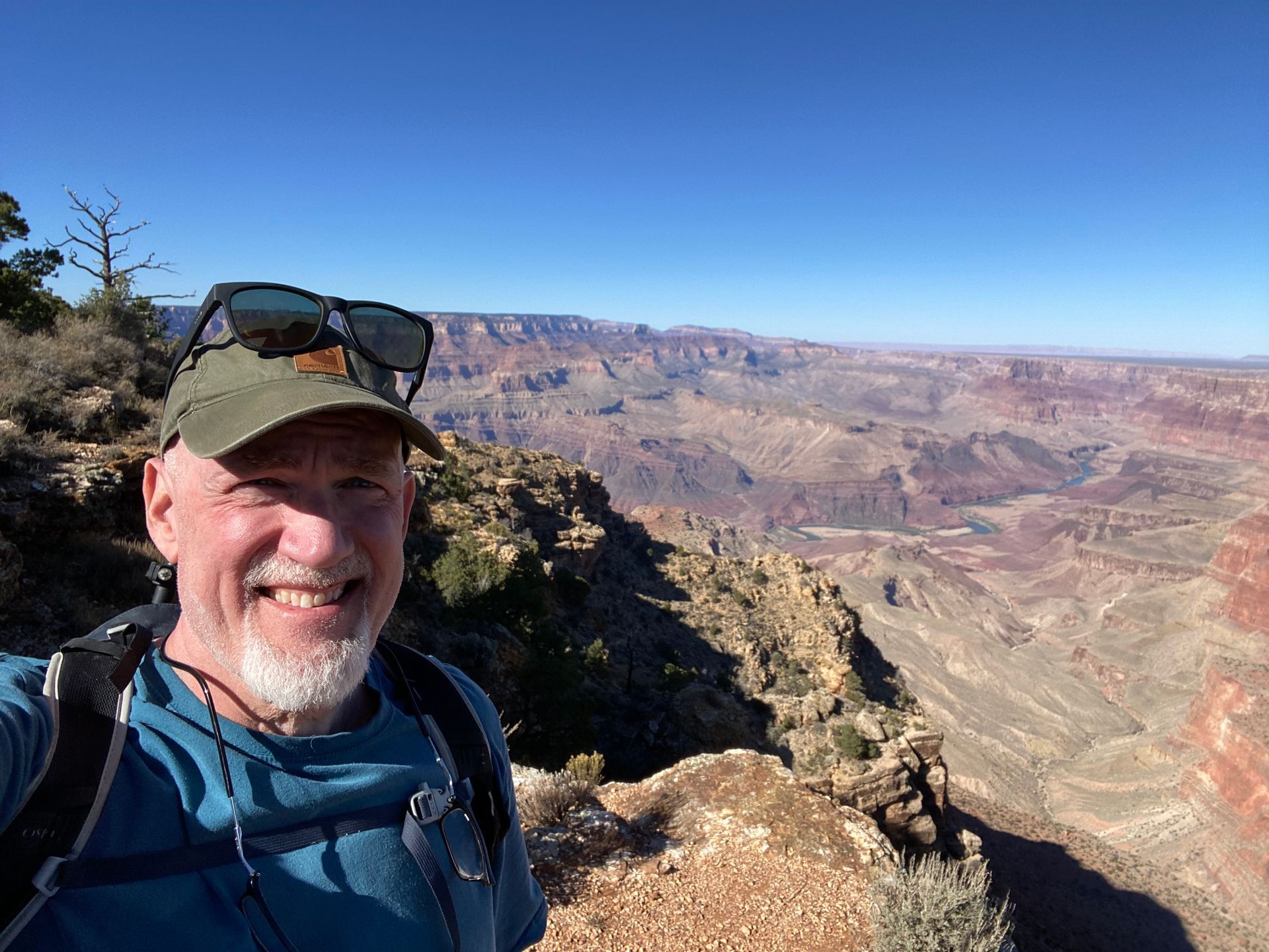 Man smiling, standing at Grand Canyon rim. Clear blue sky, canyon views.