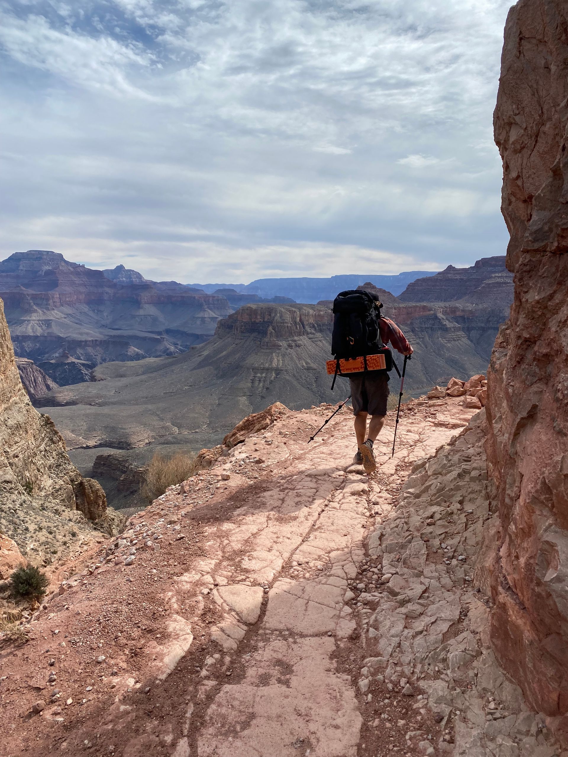 A person with a backpack is walking down a dirt path.