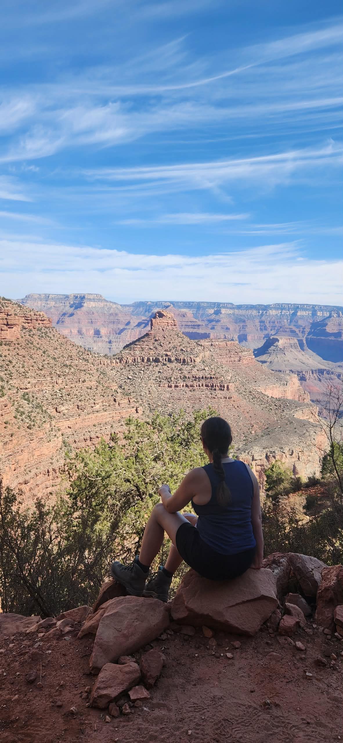Person sitting on a rock overlooking the Grand Canyon with blue sky and clouds.