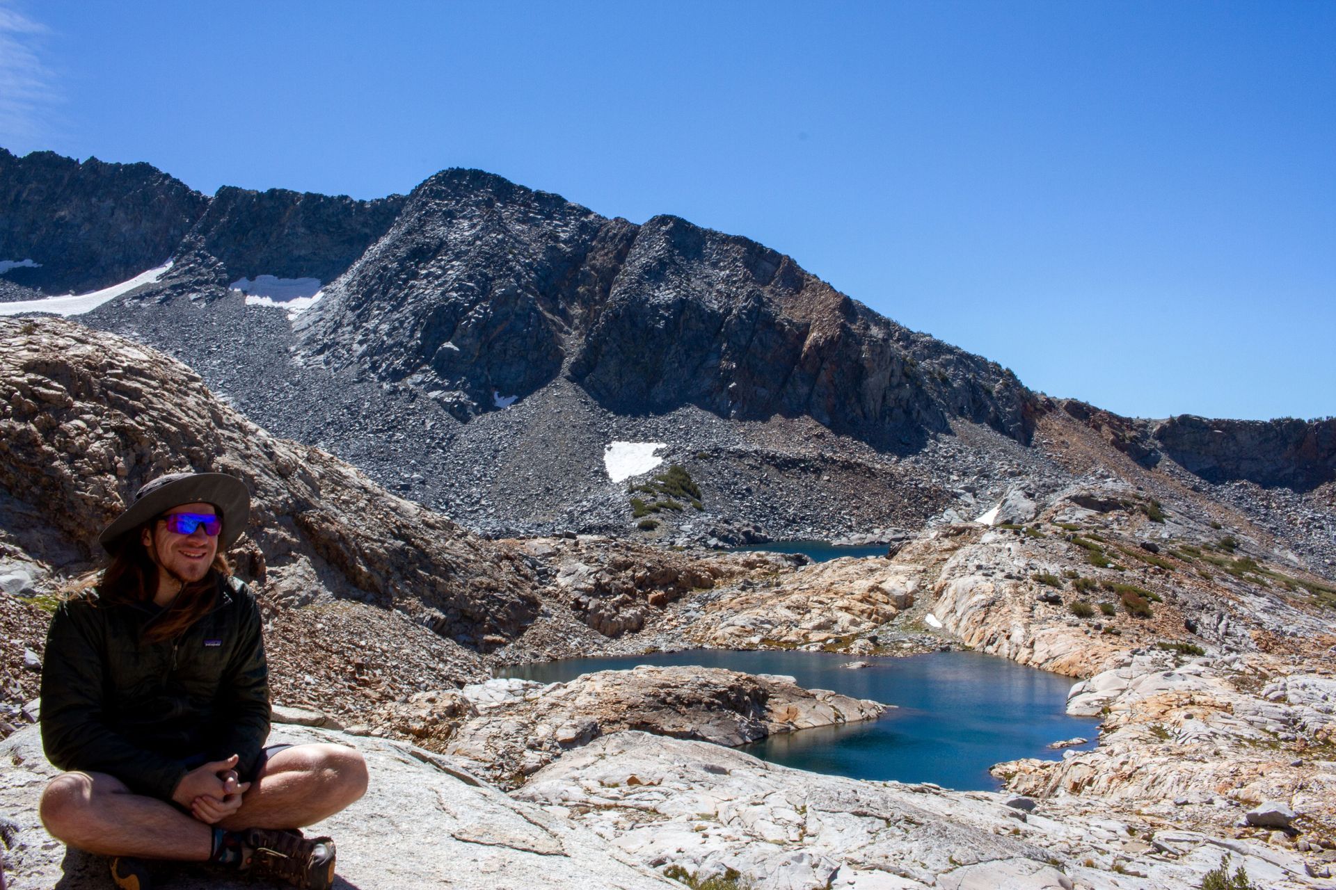 A man is sitting on a rock near a lake in the mountains.
