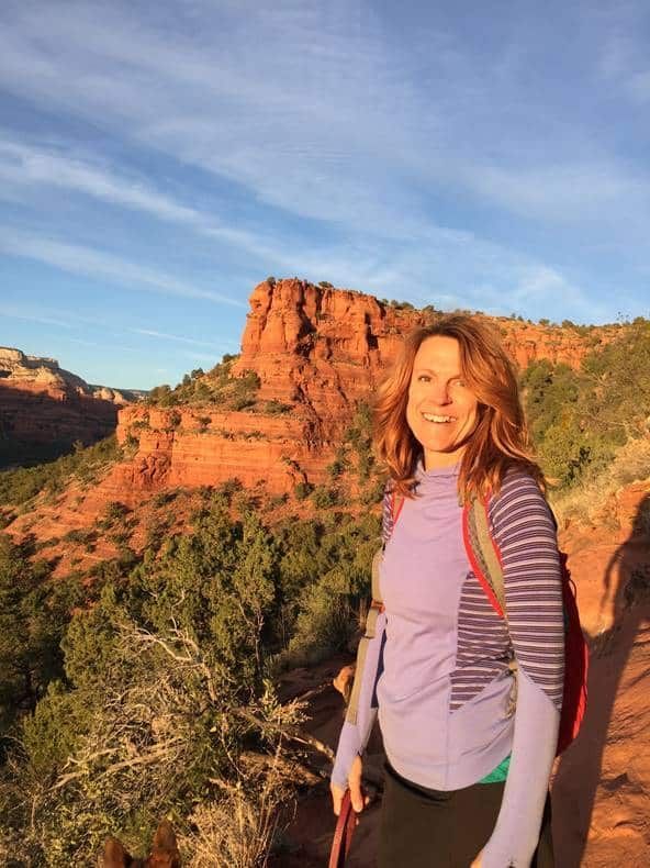 A woman with a backpack is standing in front of a mountain.