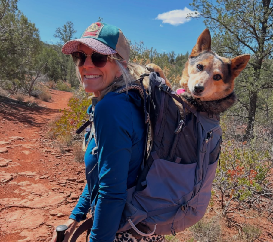 A woman with a backpack is standing in front of a mountain.