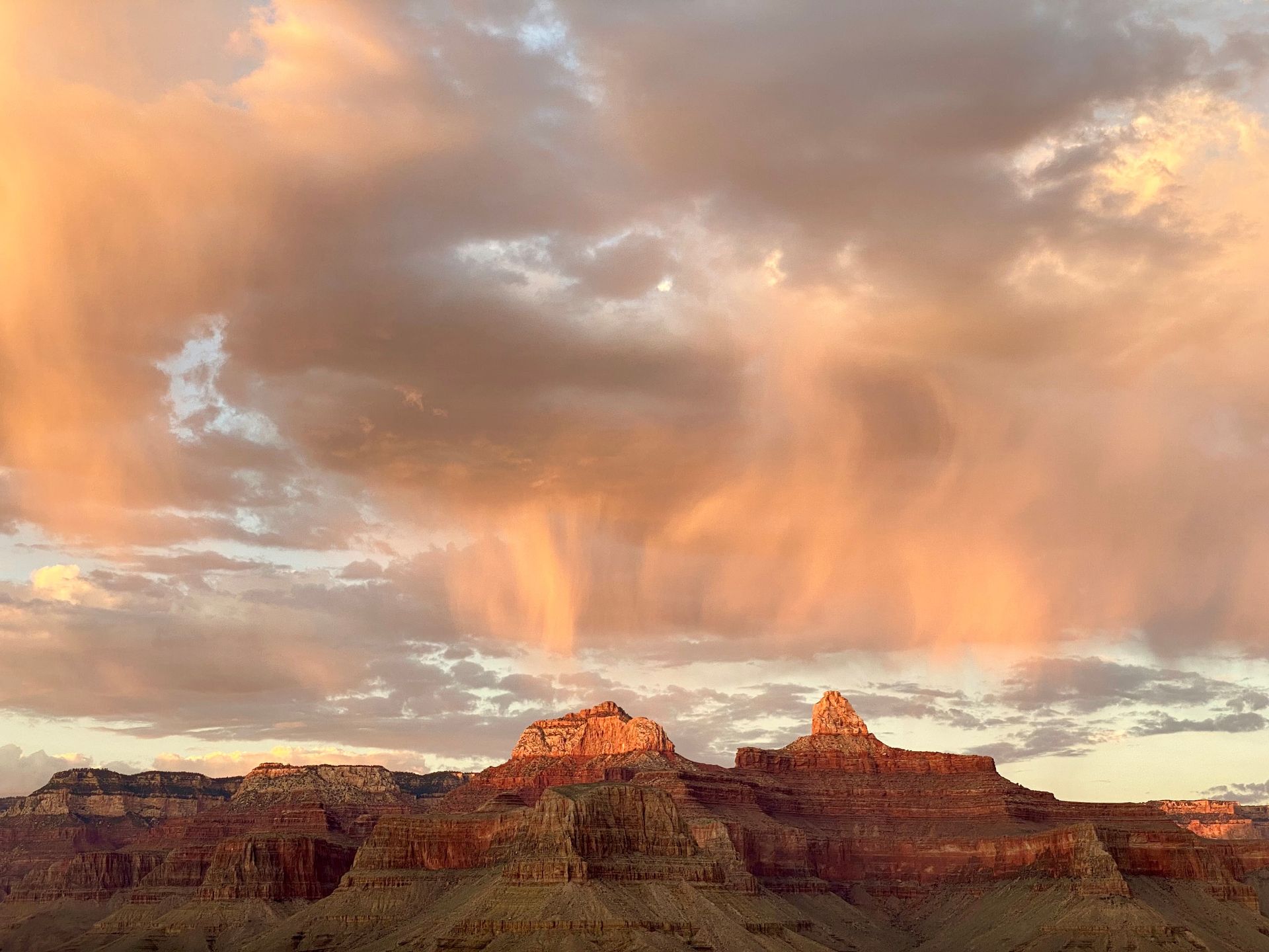 A sunset over the grand canyon with a cloudy sky and mountains in the foreground.