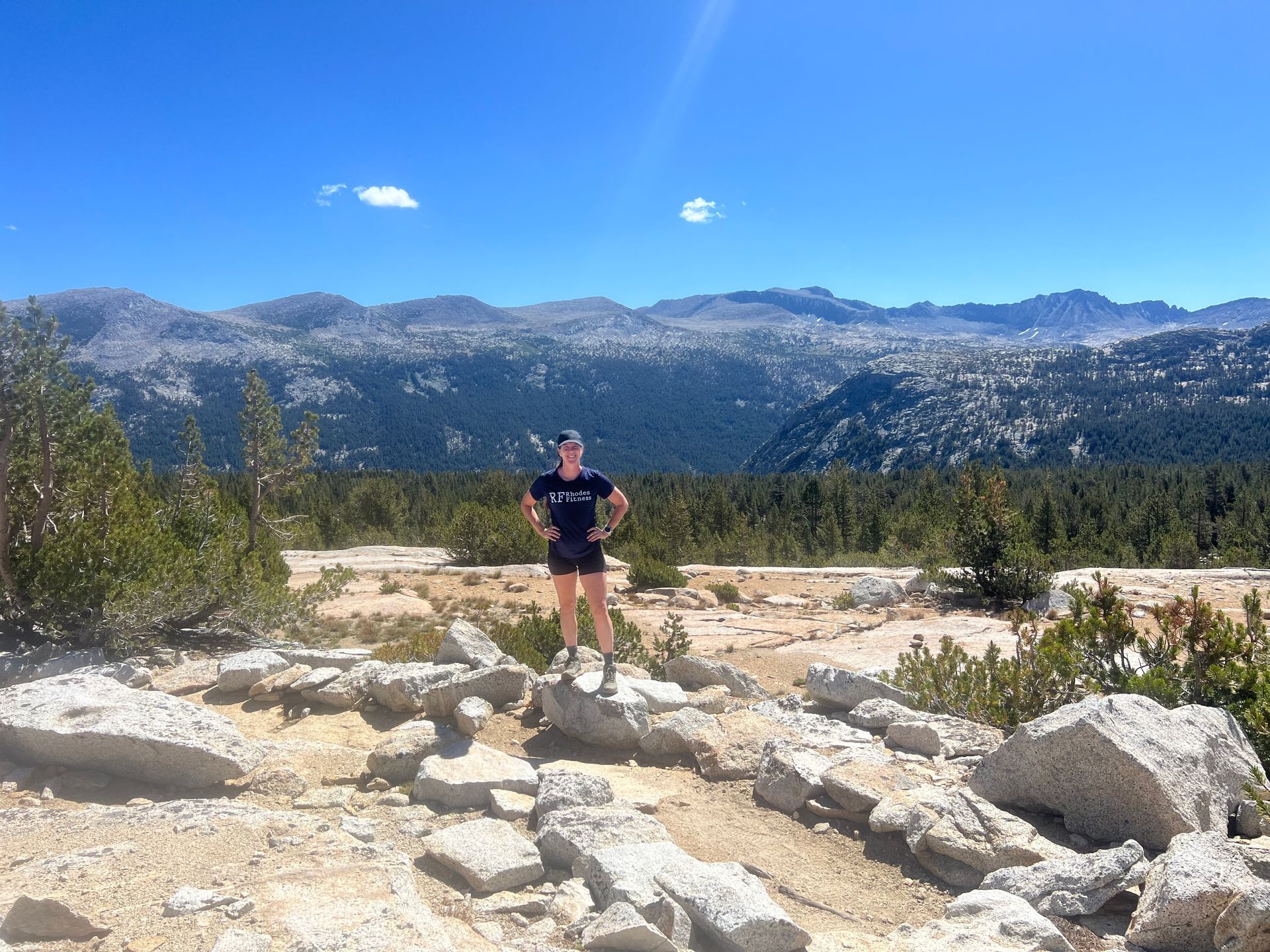 Person standing on rocks, mountain backdrop. Sunny day, blue sky.