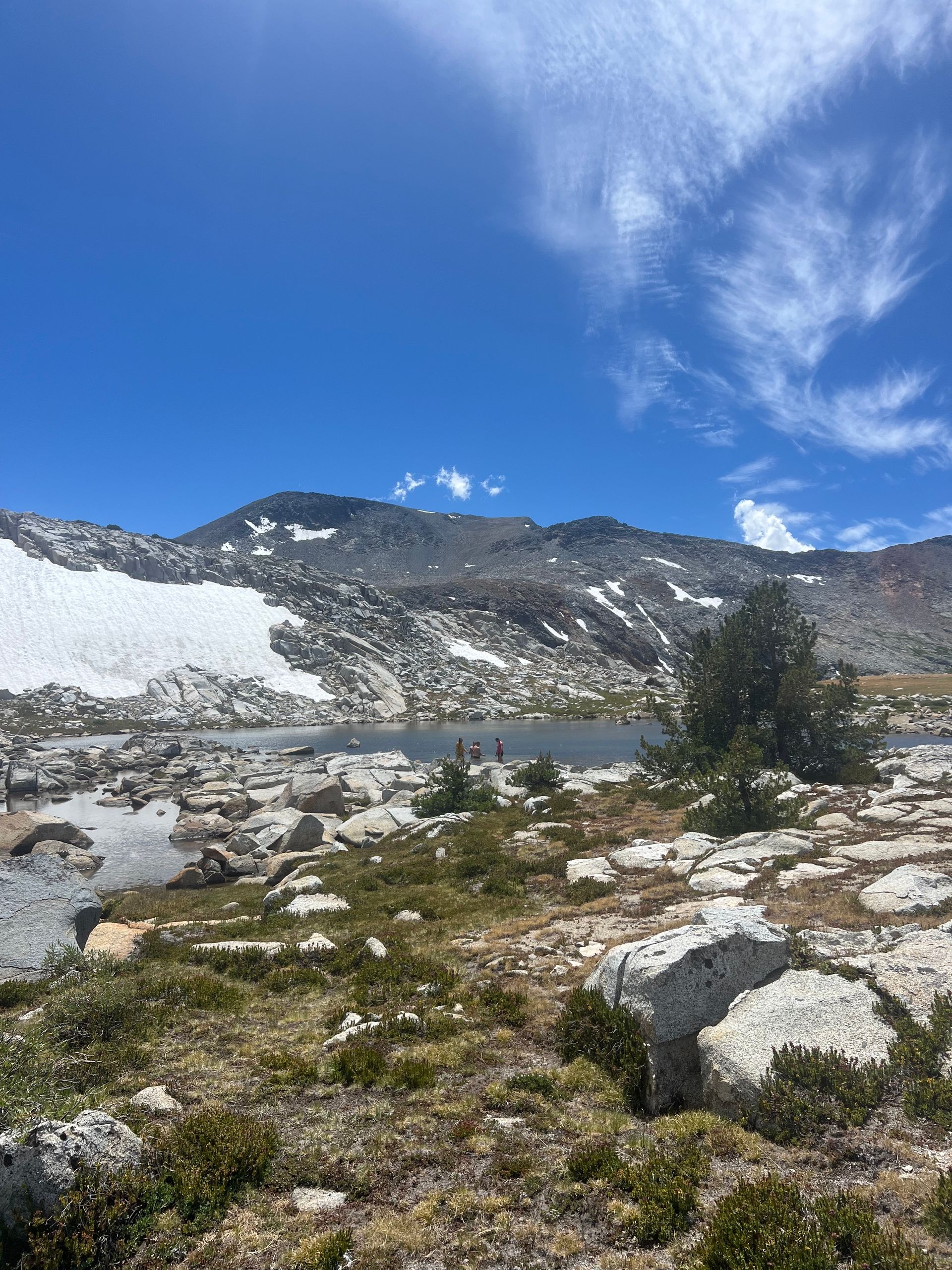 Mountain lake landscape with snow patches, rocky terrain, and blue sky with clouds.