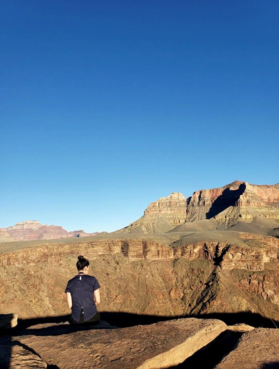 A woman is sitting on a rock overlooking a canyon.