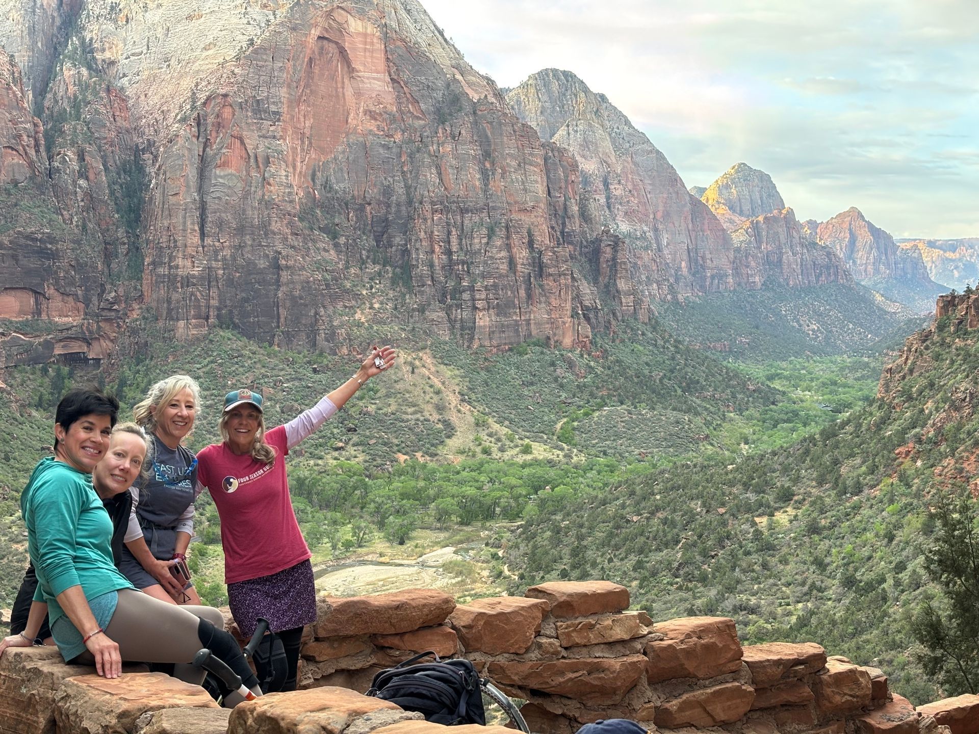 Four women pose on a stone wall overlooking a canyon, mountains in the background.
