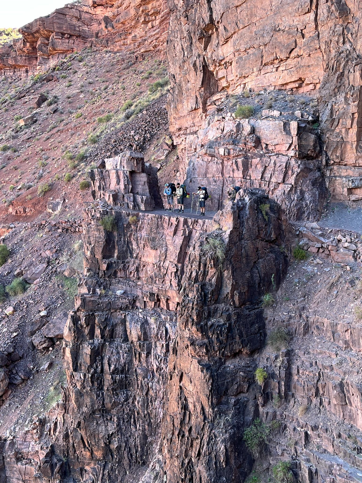 Rocky cliffside with three people standing on a small ledge.