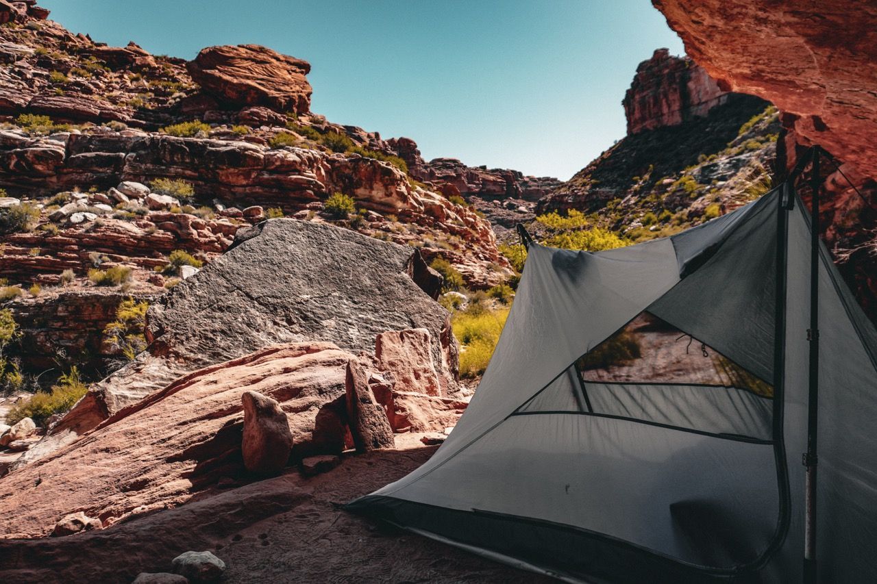 A tent is sitting in the middle of a canyon in the mountains.