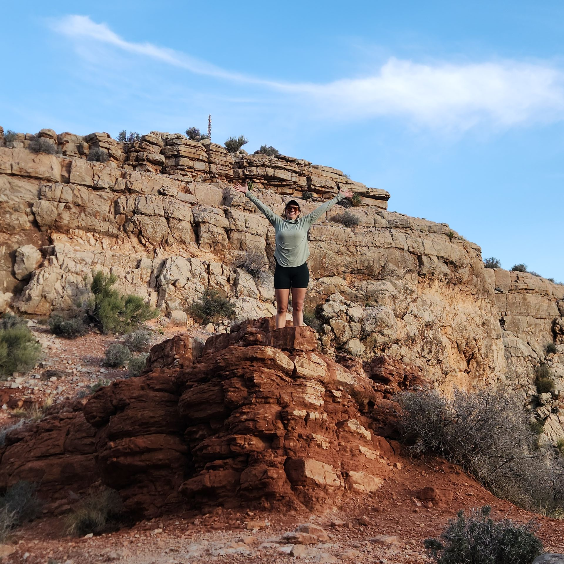 Person hanging off a rocky cliff, blue sky.