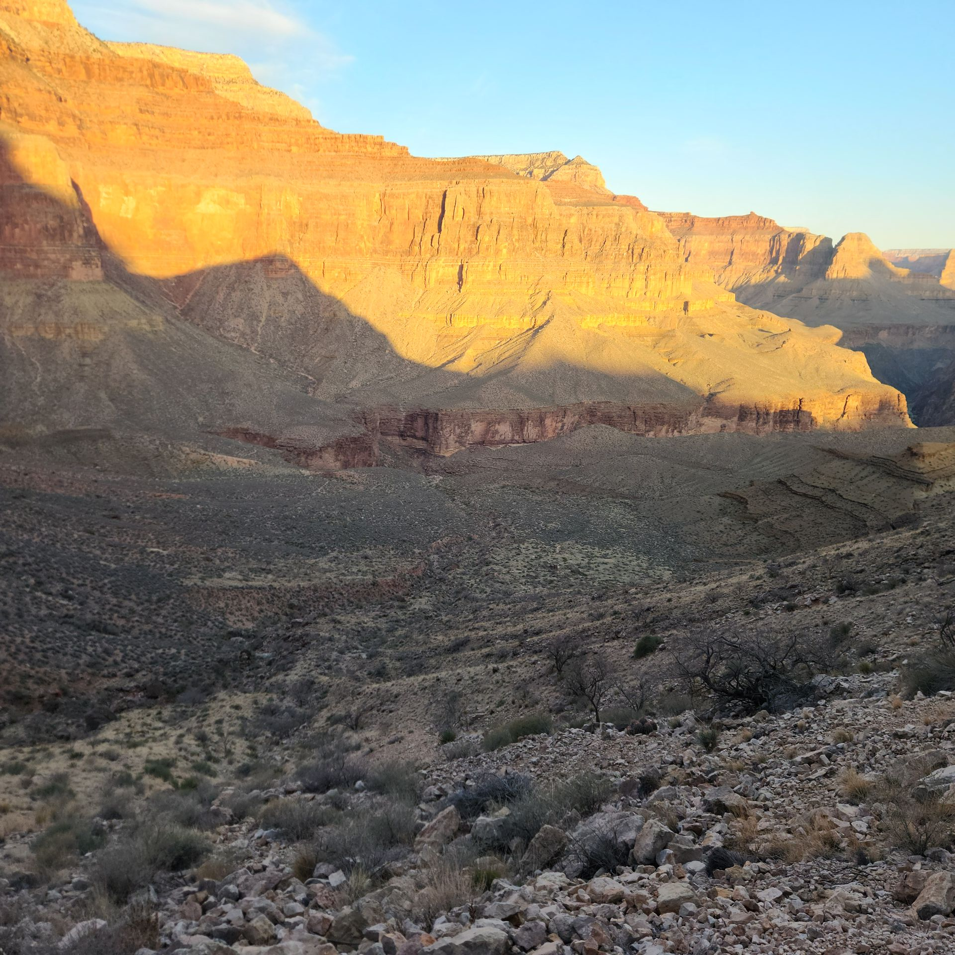 Sunlit canyon walls. The right side is a dark, rocky slope. Blue sky in the top left corner.