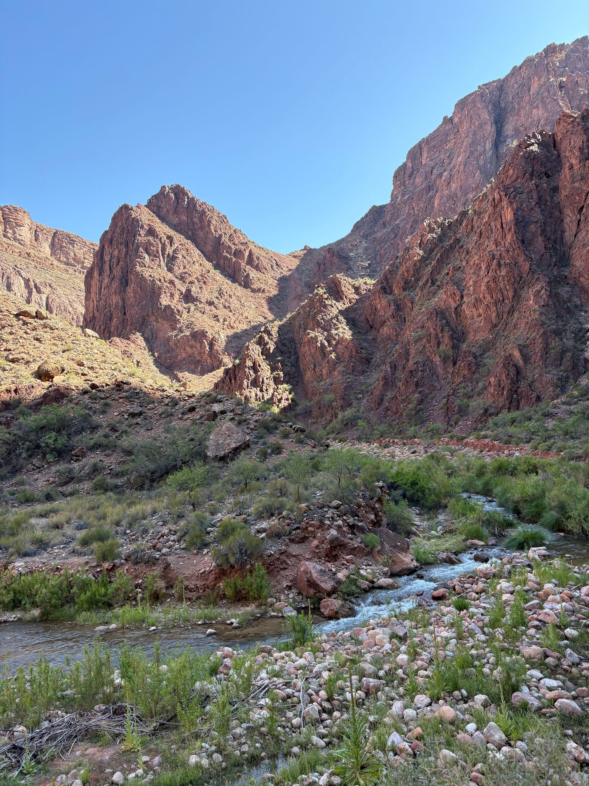 Canyon landscape with a flowing stream in foreground. Rugged rock formations, blue sky.