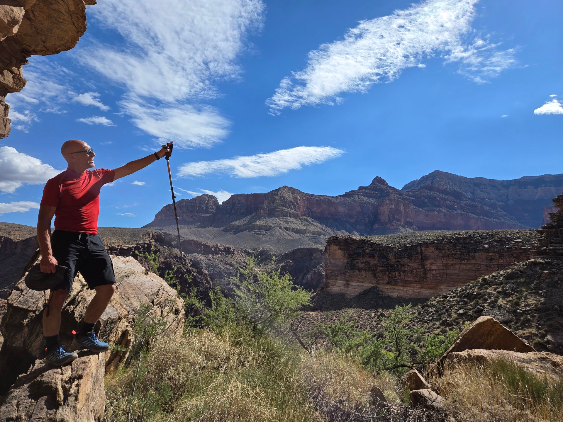 A man is standing on top of a rocky cliff with mountains in the background.