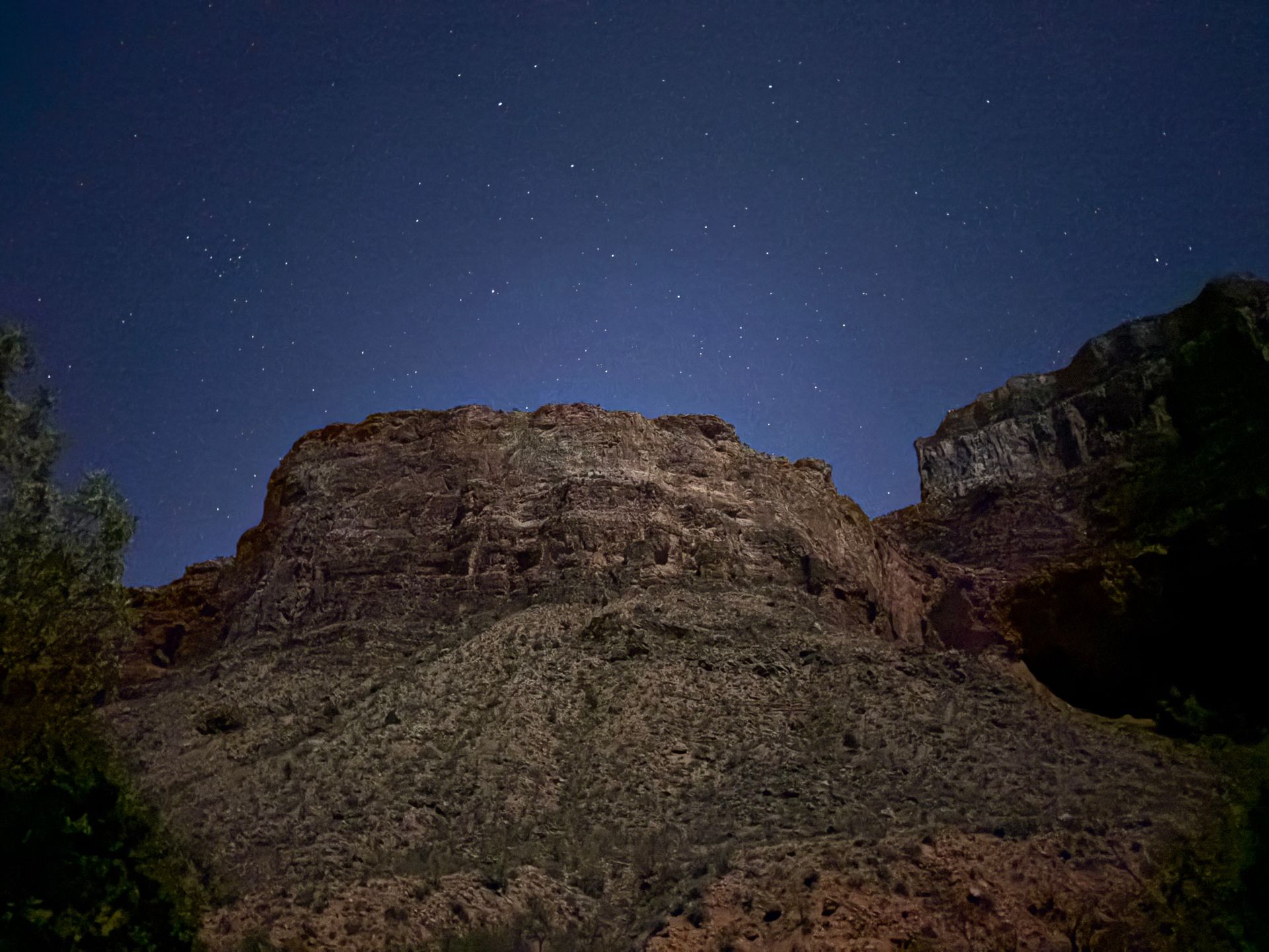 Dark sky over a rocky cliffside, illuminated by starlight.
