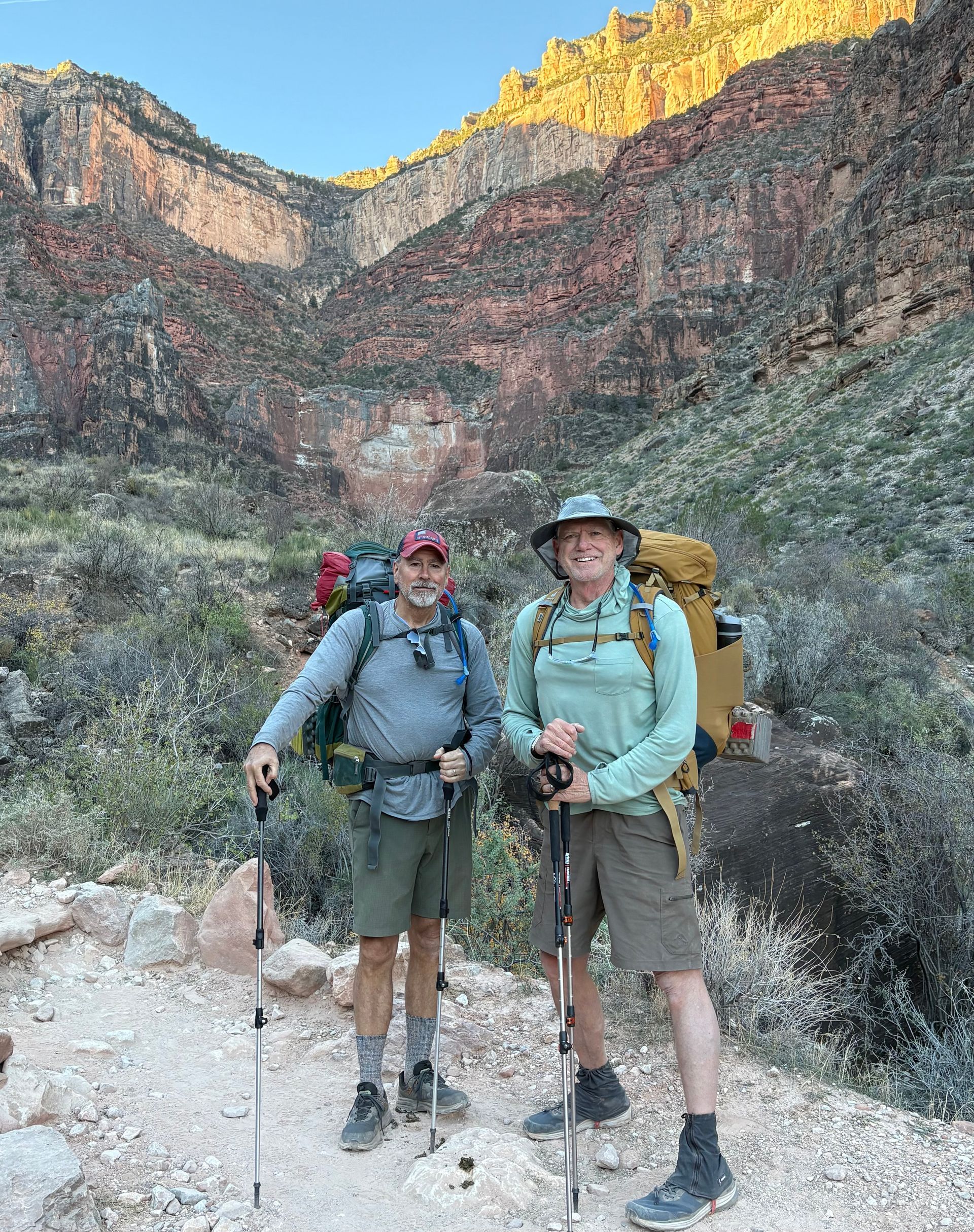 Two hikers with packs and poles pose on a trail in a canyon.