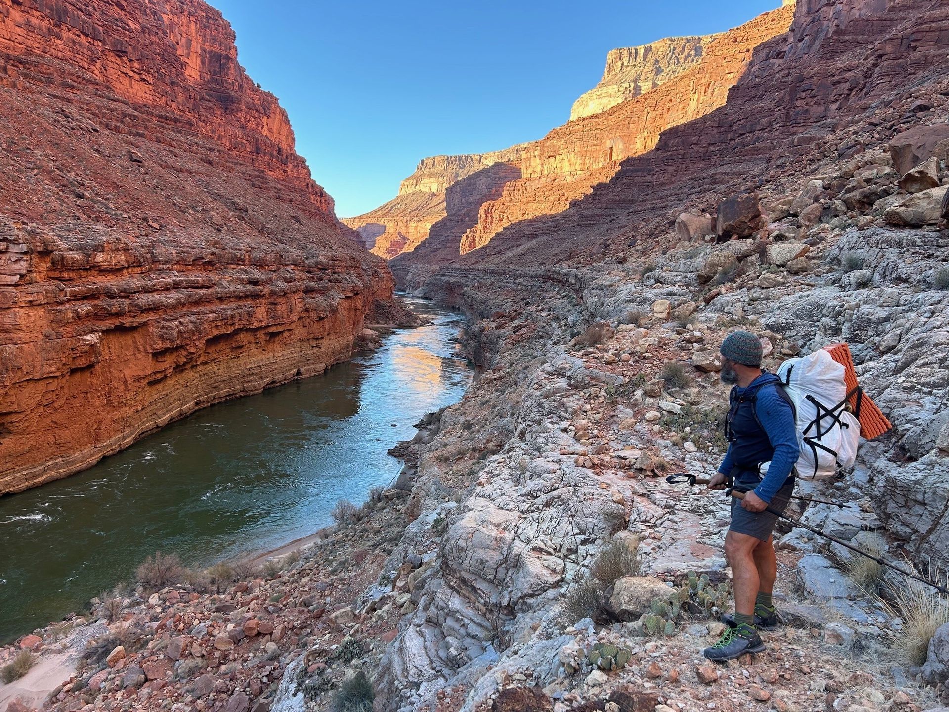A man with a backpack is standing next to a river in a canyon.