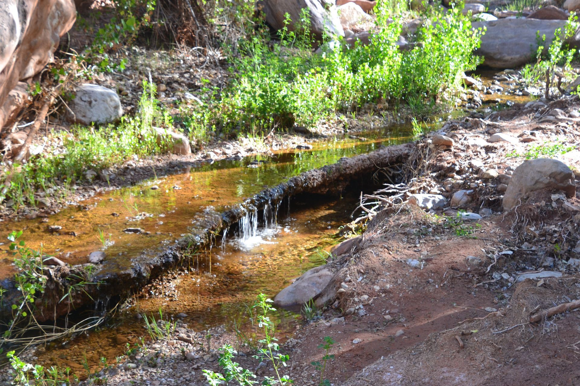 A small stream flowing through a rocky, dry landscape with green vegetation along the banks.
