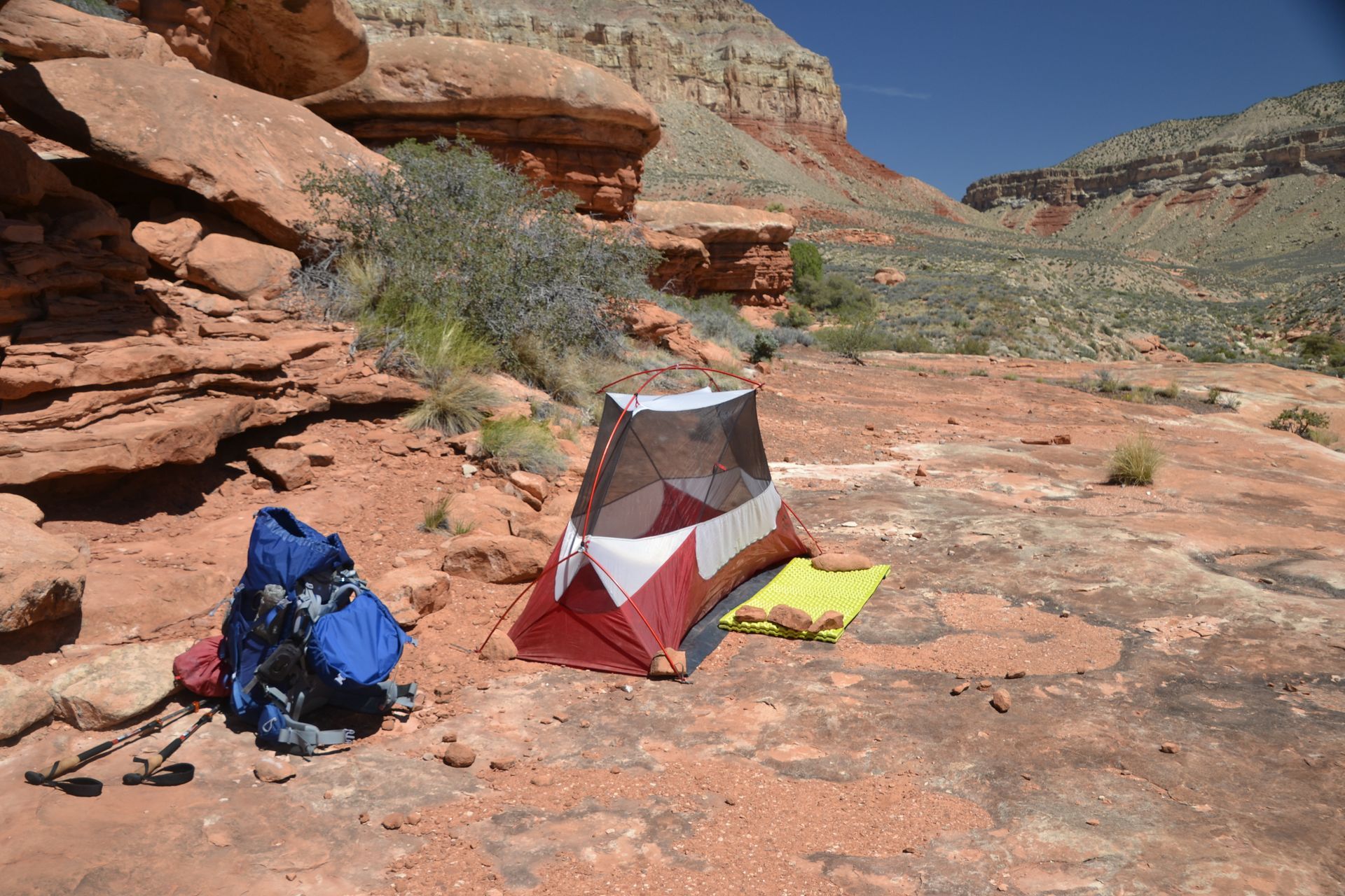 Red and white tent set up on red rock in a canyon setting, with backpack and sleeping pad.