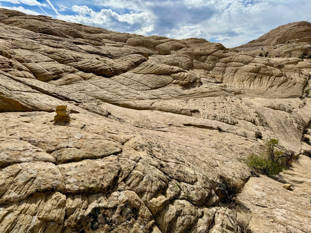 Tan, textured sandstone landscape under a cloudy sky. Small wooden marker sits on the rock.
