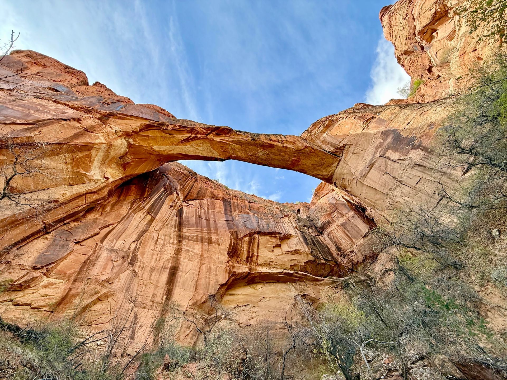 Natural sandstone arch against a partly cloudy blue sky.