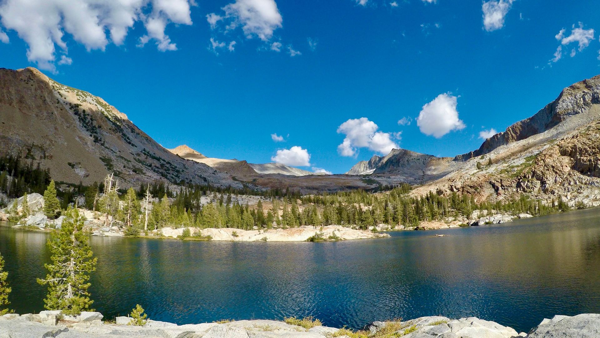 A lake surrounded by mountains and trees on a sunny day