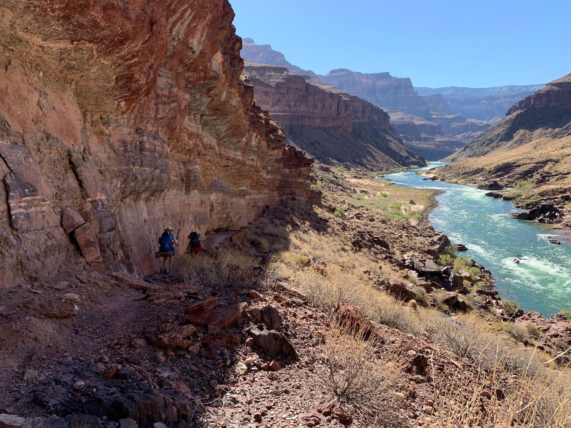 A couple of people are walking down a trail next to a river.