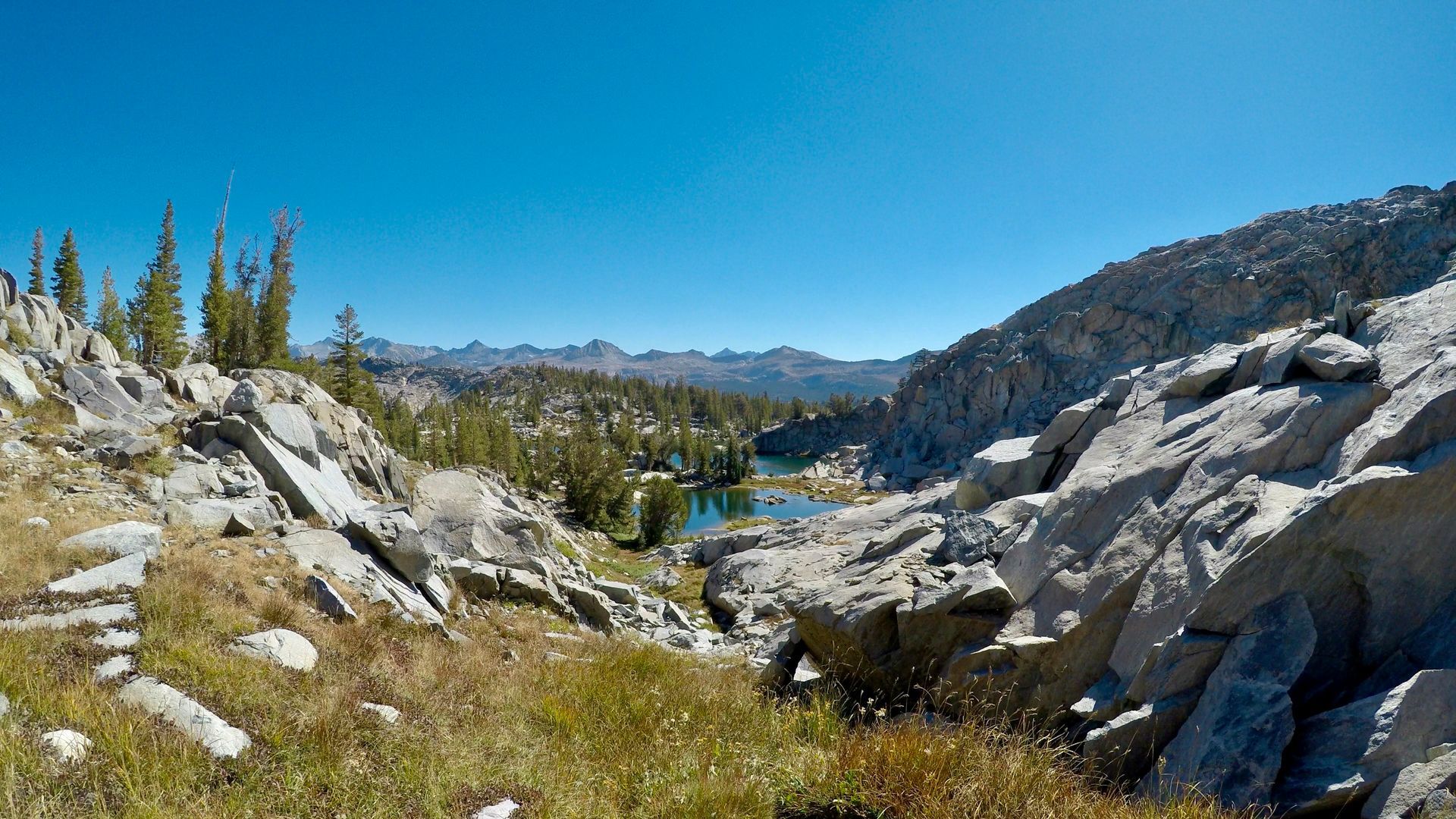There is a lake in the middle of the mountains surrounded by rocks and trees.