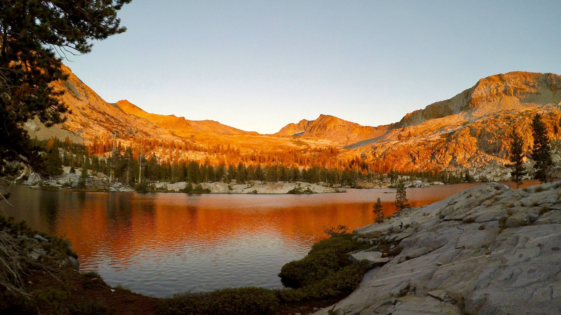 A lake in the mountains with mountains in the background at sunset.