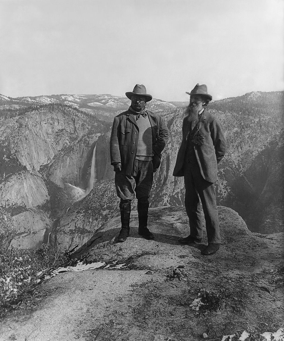 Two men are standing on top of a rocky cliff overlooking a waterfall.