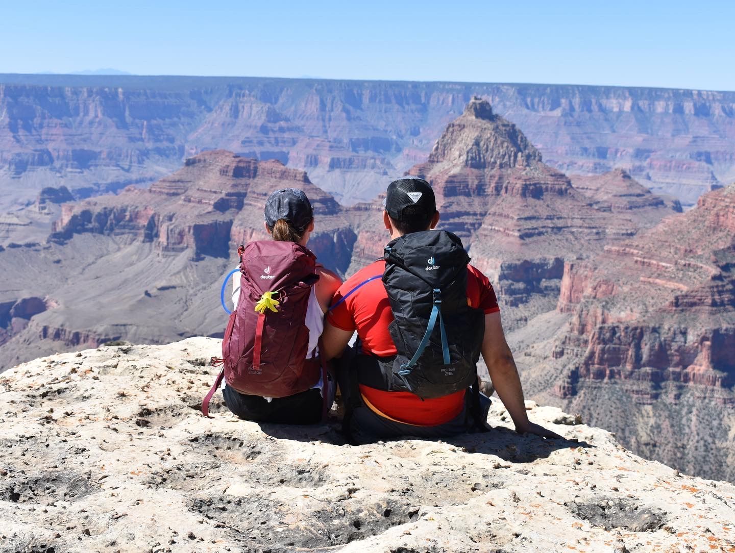 A man and a woman are sitting on top of a rock overlooking the grand canyon.