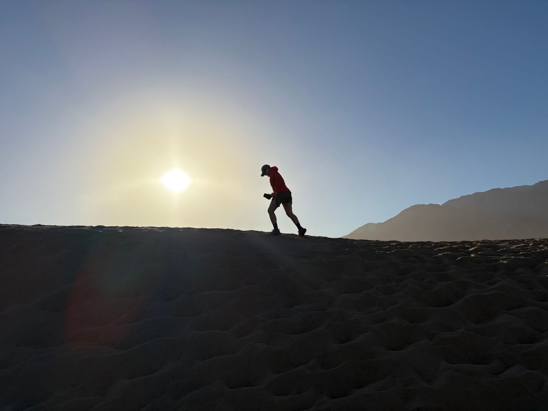Runner on beach silhouetted by bright sun. Mountains in distance.