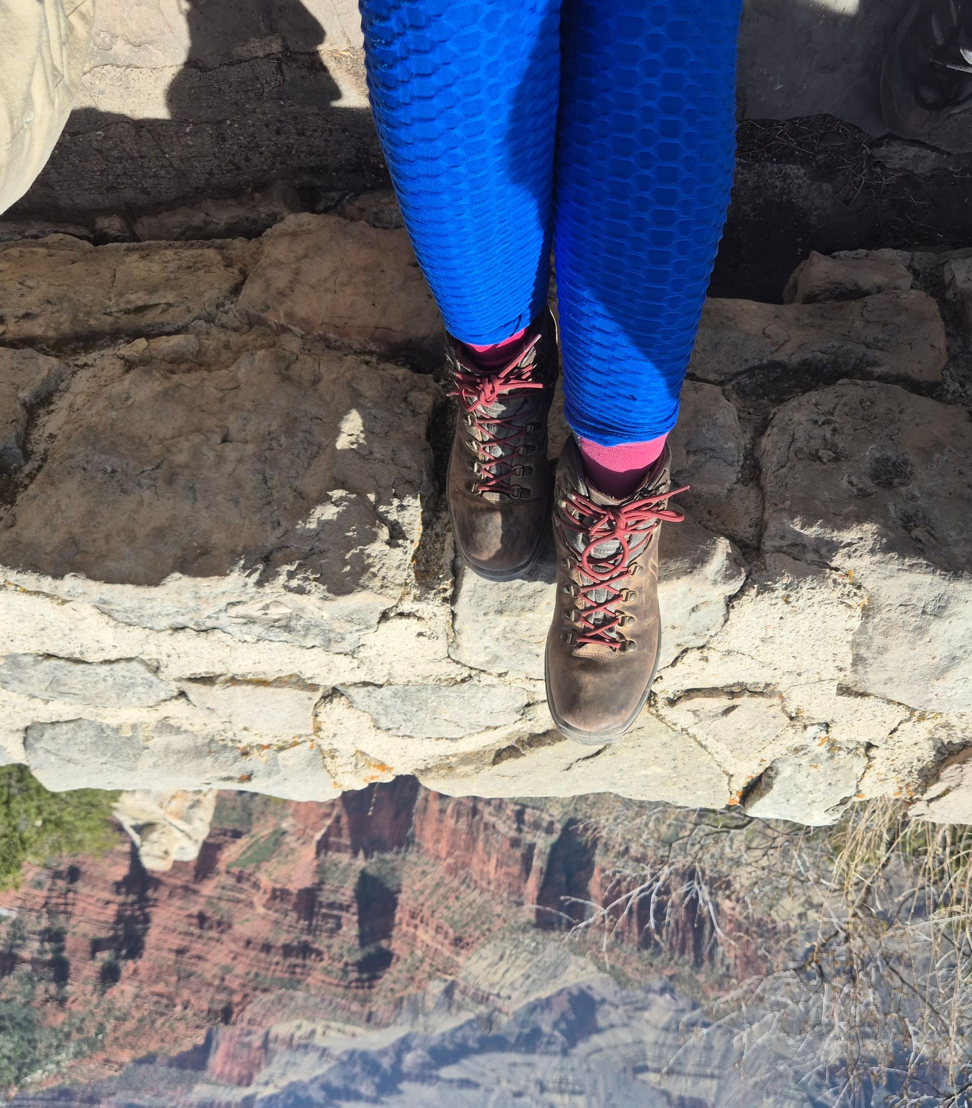 Person wearing blue leggings and hiking boots on a stone ledge overlooking a canyon.