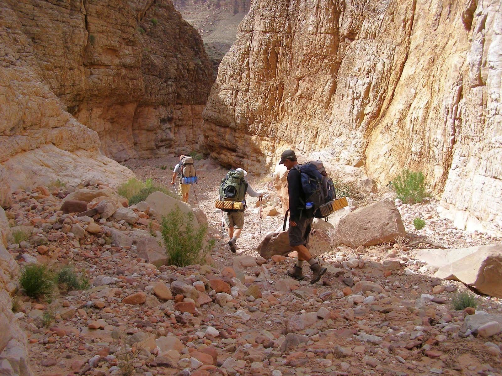 A man with a backpack is walking down a rocky trail.