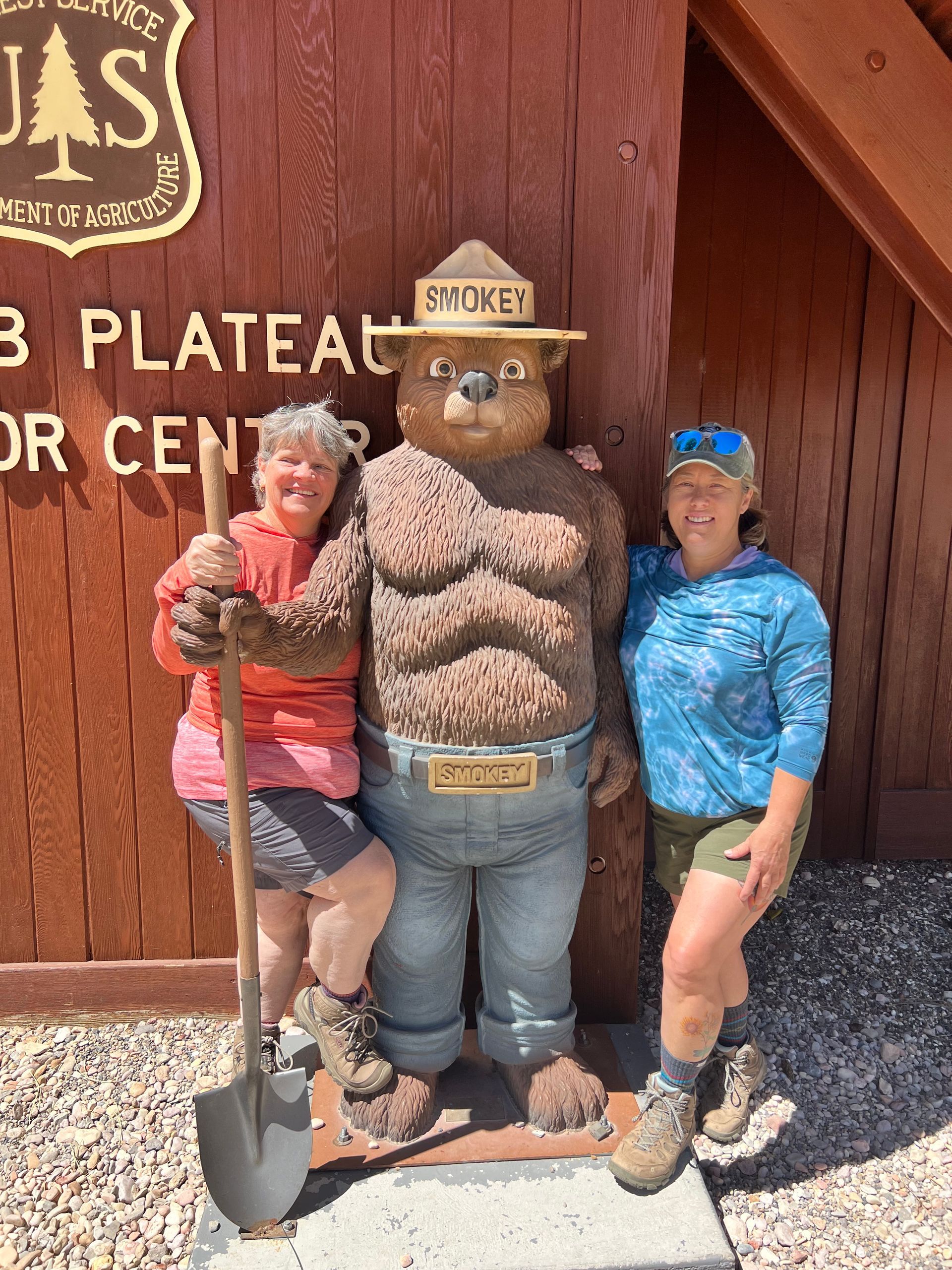 Two people pose with a Smokey Bear statue in front of a visitor center.