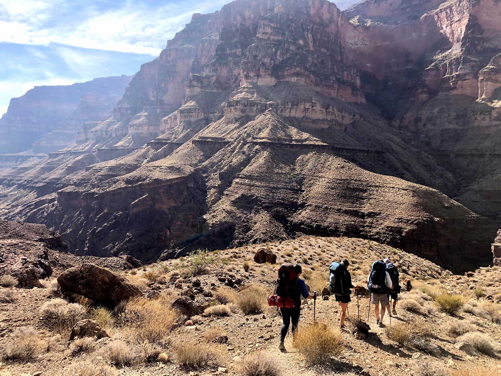 A group of people are hiking in the desert with backpacks.