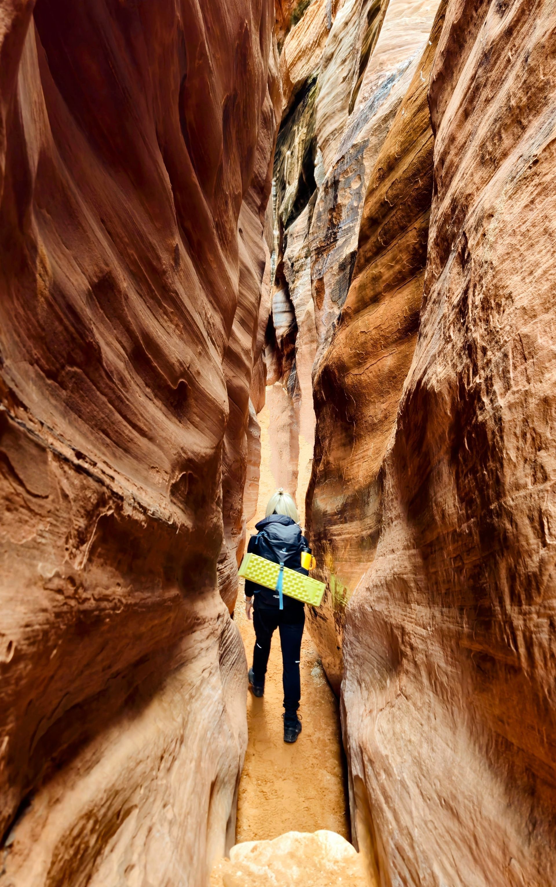 Person hikes through a narrow, sandstone slot canyon, carrying a yellow pad.